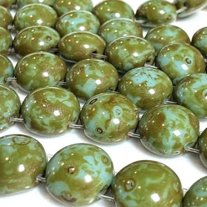 May include: Strands of olive green and teal-colored beads. The beads are round with a glossy finish and a mottled pattern. The beads are strung on a thin, silver-colored wire. The beads are likely for jewelry making.