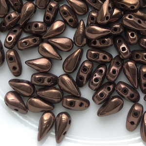 May include: A pile of small, teardrop-shaped glass beads in a metallic bronze color. The beads have two holes for stringing.