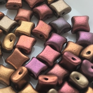May include: A pile of small, metallic, square-shaped beads in shades of copper, bronze, and purple. The beads have a slightly rounded, irregular shape and a matte finish.