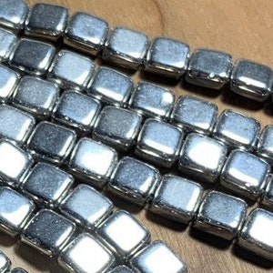 May include: A strand of silver square beads. The beads are shiny and have a metallic finish.