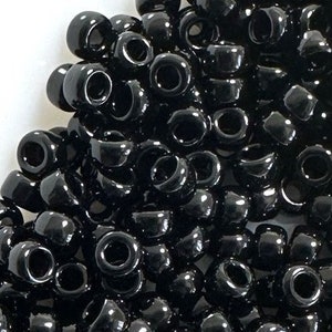 May include: A large pile of black plastic beads. The beads are round and have a hole in the center. They are commonly used for jewelry making and crafts.