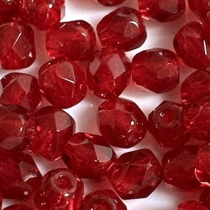 May include: A pile of red glass beads with a faceted finish. The beads are small and round, and they have a shiny, translucent appearance.