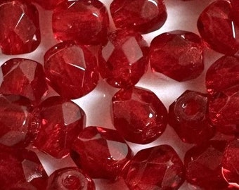 May include: A pile of red glass beads with a faceted finish. The beads are small and round, and they have a shiny, translucent appearance.