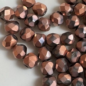 May include: A pile of copper-colored faceted glass beads. The beads are small and have a metallic sheen.