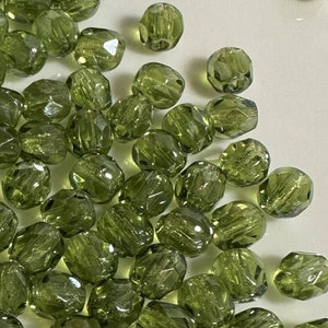 May include: A large quantity of green glass beads with a faceted, slightly irregular shape. The beads have a translucent, slightly iridescent quality.