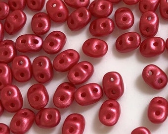 May include: A scattering of small, red, oval-shaped beads with two holes each. The beads have a glossy finish.
