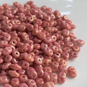 May include: A pile of small, pink, oval-shaped glass beads with a slight iridescent sheen.