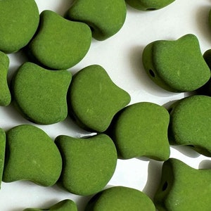 May include: A collection of green glass beads in a crescent shape. The beads have a matte finish and are scattered on a white surface.