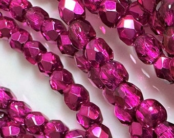 May include: A strand of magenta-colored glass beads with a metallic finish. The beads are faceted and have a slightly oval shape.