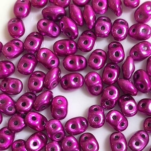 May include: A large group of small, metallic, magenta-colored beads. The beads are oval-shaped with two holes in each bead.