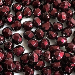 May include: A large pile of dark red faceted glass beads. The beads are shiny and have a metallic finish.
