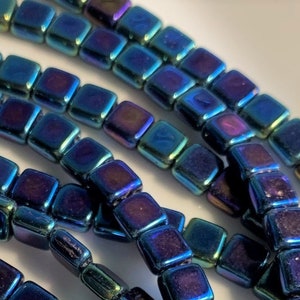 May include: A strand of iridescent blue and purple square glass beads. The beads have a metallic finish and are strung on a clear thread.
