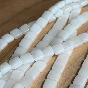 May include: A strand of white square-shaped beads. The beads are made of a smooth, opaque material and have a slightly iridescent sheen.