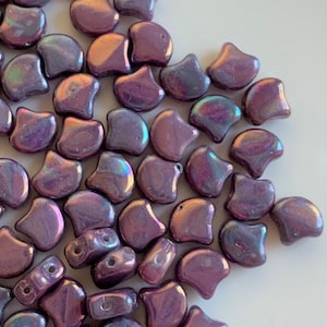 May include: A collection of iridescent purple beads with a unique, curved shape. The beads have a glossy finish and reflect multiple colors. These beads are ideal for jewelry making and crafting projects.