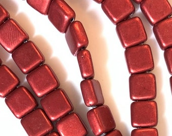 May include: A strand of red square-shaped beads. The beads are made of a matte material and have a slightly textured surface.