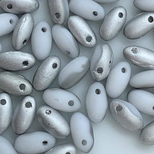 May include: A collection of white and silver oval-shaped beads with a hole in the center. The beads are arranged in a random pattern.