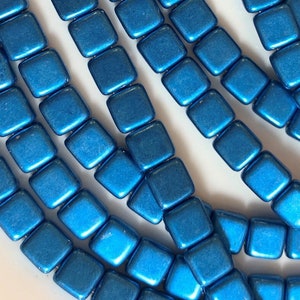 May include: A strand of blue square-shaped beads. The beads have a metallic finish and are strung together on a clear thread.