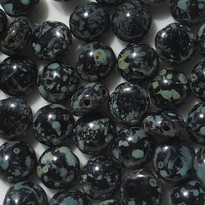 May include: A collection of black and green speckled round beads. The beads are made of glass and have a glossy finish.
