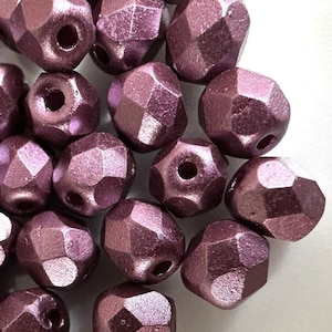 May include: A close-up of a pile of metallic purple faceted beads. The beads are small and have a shiny finish.