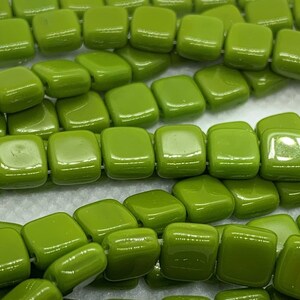May include: A strand of square-shaped green glass beads. The beads are glossy and have a smooth finish.