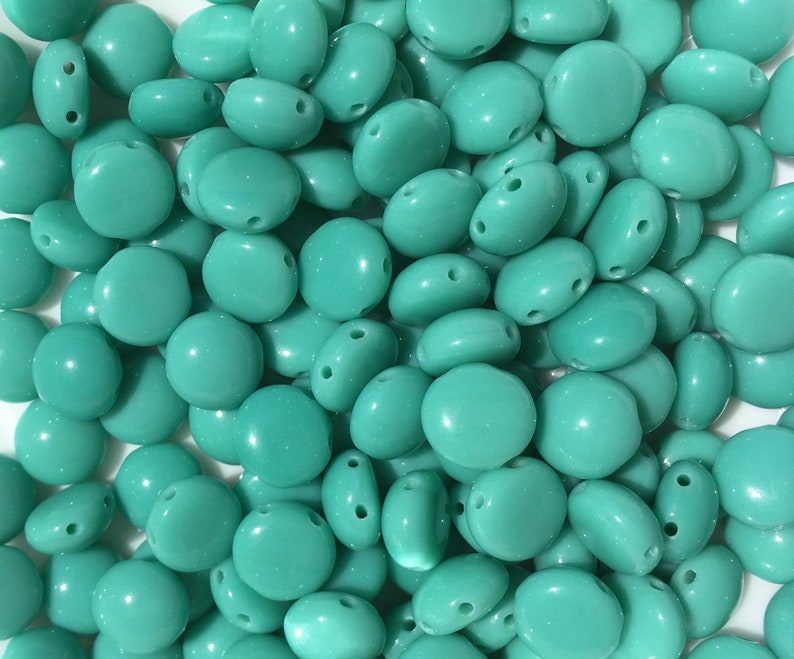 May include: A large pile of turquoise round beads with two holes in each bead.