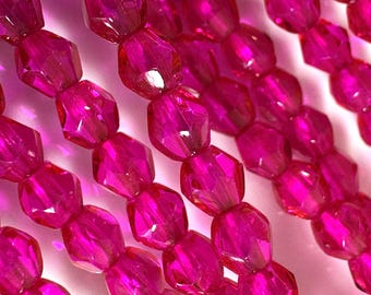 May include: Close-up of strands of faceted, hot pink beads. The beads are hexagonal in shape and have a glossy, reflective surface. The beads are strung together, creating a textured and colorful pattern. The background is a soft, light pink.