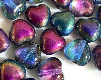 Op de afbeelding: Een verzameling iriserende hartvormige kralen. De kralen vertonen een scala aan kleuren, waaronder paars, blauw en groen, met een glanzend, reflecterend oppervlak. Ideaal voor het maken van sieraden en knutselprojecten.