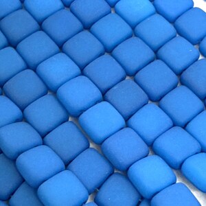 May include: Close-up of a collection of square, blue glass tiles. The tiles are arranged in a grid pattern, with varying shades of blue creating a gradient effect. The tiles have a matte finish.