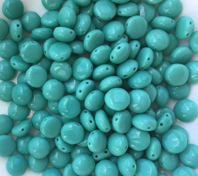 May include: A large pile of turquoise blue glass beads. The beads are round and have two holes in them.