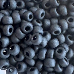 May include: A close-up of a pile of small, black seed beads. The beads are matte and have a slightly rough texture.