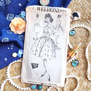 May include: Vintage dressmaking pattern from Weldons, size 16, featuring a floral design. The illustration shows a woman in a dress with a full skirt. The pattern is on a cream-colored paper, with the text "WELDONS 8094".