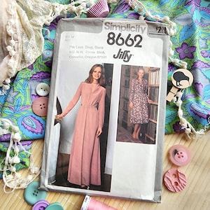 以下が含まれることがあります： ヴィンテージのSimplicity 8662ソーイングパターン、サイズ14。2つのドレスのイラストが特徴です。 パターン封筒は、生地、ボタン、キウイ型の木製洗濯バサミに囲まれています。 封筒には「Jiffy」の文字があります。