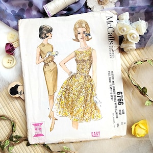 Könnte beinhalten: Vintage McCall's Schnittmuster mit Illustrationen von zwei Kleidern. Das Hauptbild zeigt ein gelbes Kleid mit floralem Muster und weitem Rock. Die Schnittmusternummer ist 6766, für einen Brustumfang von 81 cm. Das Wort "EASY" ist unten aufgedruckt.