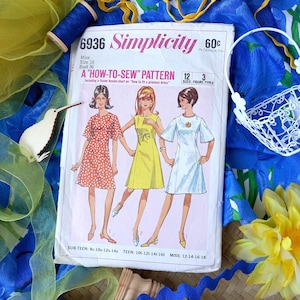 May include: A vintage Simplicity sewing pattern, number 6936, featuring illustrations of three dresses. The pattern includes sizes for Miss, Teen, and Sub-Teen figures. The cover displays the text "A How-To-Sew Pattern" and the price.