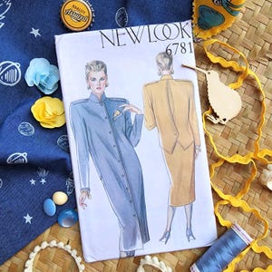 Puede incluir: Un patrón de costura New Look vintage, número 6781, con ilustraciones de un abrigo largo azul y un traje amarillo. El patrón está sobre una tela azul con diseños de estrellas y planetas, junto con elementos decorativos.