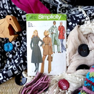 Może przedstawiać: Vintage wykrojnik krawiecki Simplicity, numer 9612, z ilustracjami płaszczy i kostiumów damskich. Wzór otoczony jest skrawkami materiału, guzikami i drewnianą figurką ptaka. Rozmiar wykroju to 12, z biustem 86 cm i talią 64 cm.