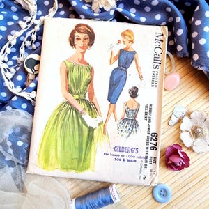 Pode incluir: Padrão de costura vintage McCall's com ilustrações de vestidos. A capa mostra um vestido verde e um azul. O texto no padrão diz "Vestido para senhoritas e juniores com saia justa ou ampla".