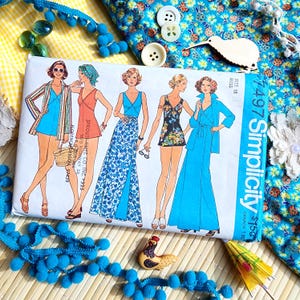 May include: A vintage Simplicity sewing pattern, size 18 Miss, featuring illustrations of women's swimwear and dresses. The pattern is surrounded by blue pom-pom trim, buttons, and a wooden kiwi bird.
