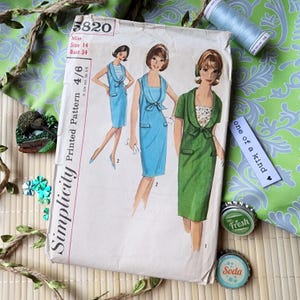 Puede incluir: Patrón de costura Simplicity vintage, talla 14, con ilustraciones de vestidos azules y verdes. El sobre del patrón va acompañado de una bobina de hilo, tapones de botella y una etiqueta que dice "one of a kind". Contorno de pecho 86 cm.