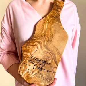 Peut inclure: Une planche à découper en bois avec un motif de grain de bois naturel. La planche a une poignée et est gravée avec le texte "Die geheime Zutat ist immer Liebe Andy & Julia".