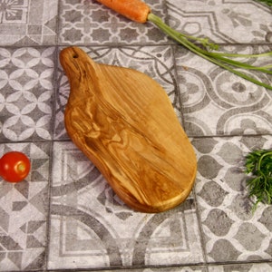 Peut inclure: Une planche à découper en bois naturel avec une forme organique unique et une poignée. La planche est de couleur brun foncé avec un motif de grain.