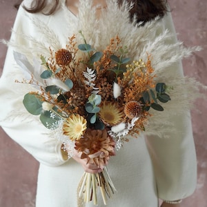 May include: A dried flower bouquet with pampas grass, eucalyptus, and dried flowers in shades of brown, beige, and white.