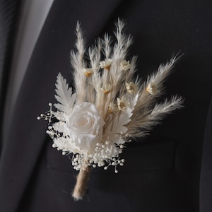 Op de afbeelding: Een witte roos met gedroogd pampasgras en baby's adem, een populaire keuze voor bruiloftscorsages.