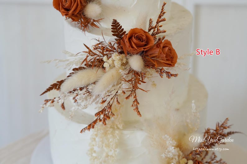 May include: A multi-tiered white cake decorated with rust-colored roses, dried ferns, and cream-colored bunny tail grass. The text Style B is visible in red, and the text MissYouGarden https://www.etsy.com is visible in white script.
