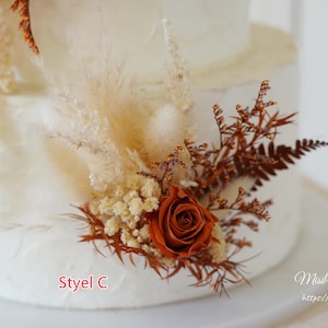 May include: A white tiered cake decorated with dried floral arrangements featuring a rust-colored rose, beige pampas grass, cream-colored baby's breath, and brown fern fronds. The text "Styel C" and "MissYouGarden https://www.etsy.com" are visible.