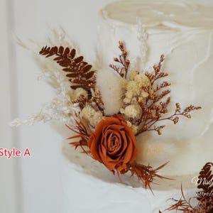 May include: A white frosted cake decorated with dried floral arrangements featuring rust-colored roses, brown ferns, and cream-colored pampas grass. The text Style A and MissYouGarden https://www.etsy.com are visible on the image.