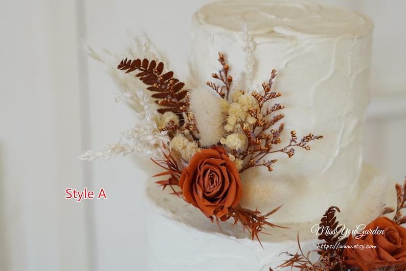 May include: A white frosted cake decorated with dried floral arrangements featuring rust-colored roses, brown ferns, and cream-colored pampas grass. The text Style A and MissYouGarden https://www.etsy.com are visible on the image.