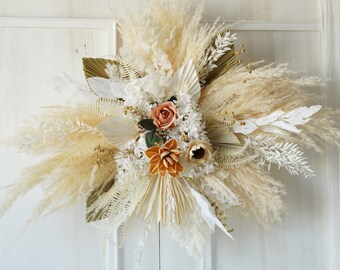 May include: A dried floral arrangement with white pampas grass, dried palm leaves, and peach-colored roses. The arrangement is perfect for a boho-chic wedding or home decor.
