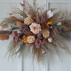 May include: A dried floral arrangement featuring a mix of beige, pink, and brown flowers and grasses. The arrangement is in a rustic style and would be ideal for a wedding or other special event.