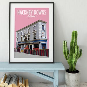 May include: A pink and gray illustration of a pub called "The Hackney Downs" in East London. The pub has a gray facade with a pink awning and a sign that says "The Hackney Downs" in white letters. The pub is surrounded by a fence with colorful stripes.